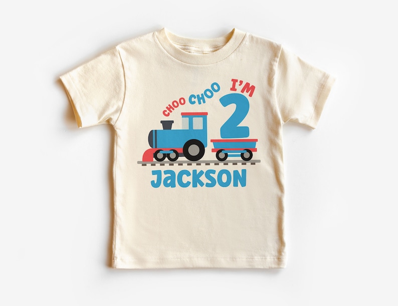 May include: A cream colored t-shirt with a blue train and red caboose. The train says "Choo Choo I'm 2" and the name "Jackson" is printed below the train.