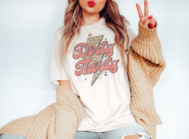 May include: A white t-shirt with a pink and brown graphic that says "Dirty Thirty" with a leopard print lightning bolt design.