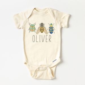 May include: A cream-colored baby onesie with a green, yellow, and blue bug design and the name "OLIVER" printed in black.
