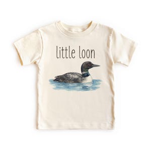May include: A cream-coloured t-shirt with a watercolour illustration of a loon in blue water. The text "little loon" is printed above the bird. The shirt is made of a soft material.