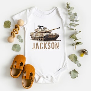 May include: White baby onesie with a camouflage tank printed on the front. The onesie has the name "JACKSON" printed below the tank.