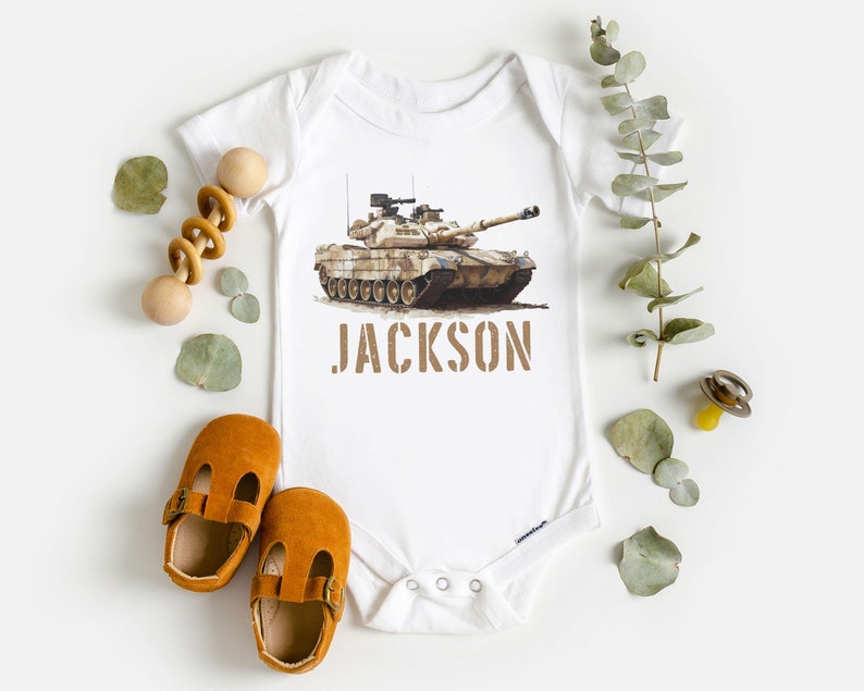 May include: White baby onesie with a camouflage tank printed on the front. The onesie has the name "JACKSON" printed below the tank.
