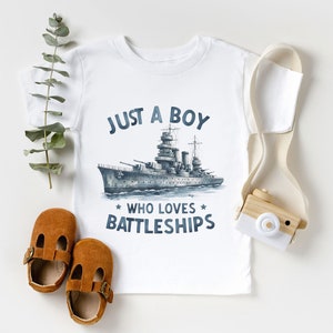 May include: White t-shirt with a blue and grey illustration of a battleship and the text "Just a boy who loves battleships".