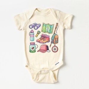K&ouml;nnte beinhalten: Cremefarbener Baby-Body mit einer farbenfrohen Illustration von Wander- und Campingausr&uuml;stung. Das Design umfasst ein Fernglas, eine Karte, Wanderschuhe, einen Rucksack, einen Kompass, eine Wasserflasche und ein Glas mit einem Marienk&auml;fer.