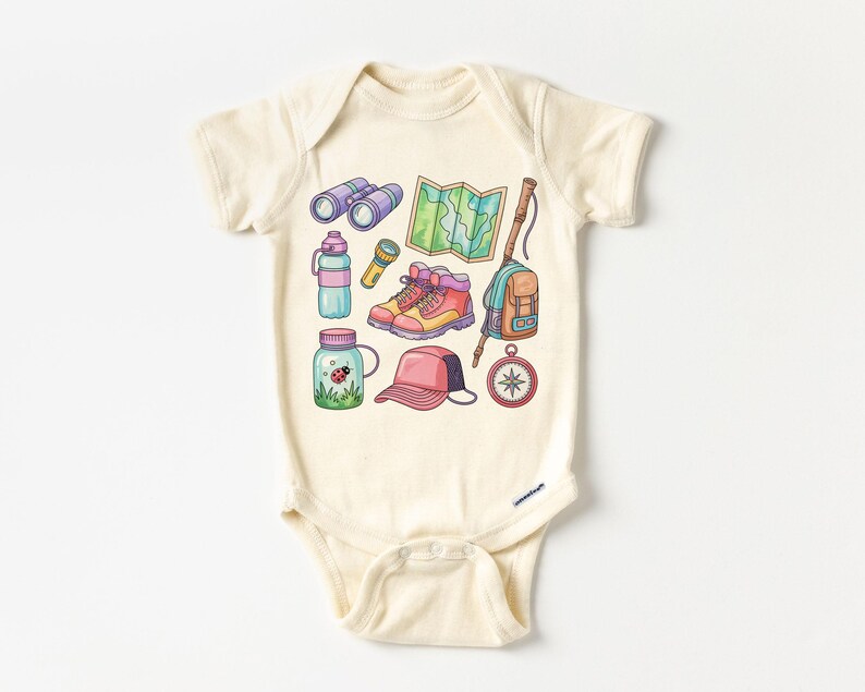 K&ouml;nnte beinhalten: Cremefarbener Baby-Body mit einer farbenfrohen Illustration von Wander- und Campingausr&uuml;stung. Das Design umfasst ein Fernglas, eine Karte, Wanderschuhe, einen Rucksack, einen Kompass, eine Wasserflasche und ein Glas mit einem Marienk&auml;fer.