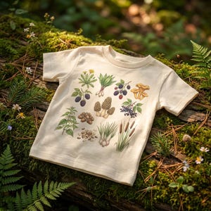 May include: Cream-colored t-shirt featuring a botanical illustration of various plants and fungi, including mushrooms, berries, and herbs. The design is printed on a short-sleeved shirt, perfect for nature lovers and those interested in botany.