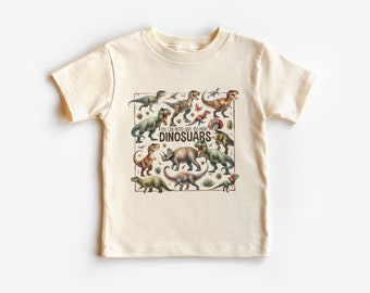 Könnte beinhalten: Ein hellbeiges T-Shirt mit einem grafischen Druck verschiedener Dinosaurier in einem quadratischen Rahmen. Der Text "You can never have too many DINOSAURS" ist in der Mitte des Rahmens gedruckt.