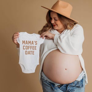 Puede incluir: Un body blanco de manga corta para beb&eacute; con el texto MAMA'S COFFEE DATE impreso en una fuente marr&oacute;n en la parte delantera. La prenda est&aacute; confeccionada en un tejido suave e incluye un cuello tipo sobre y cierres a presi&oacute;n en la entrepierna.