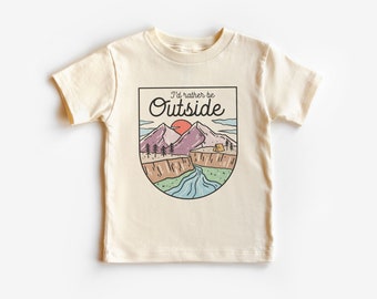 May include: A cream colored t-shirt with a graphic of a mountain range, a river, a tent, and a setting sun. The text "I'd rather be Outside" is written in a cursive font above the graphic.