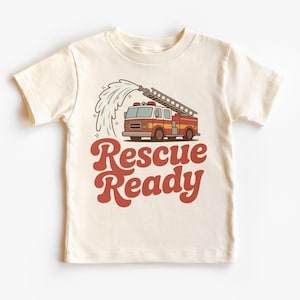 May include: Cream-colored t-shirt featuring a retro-style illustration of a fire truck with a ladder and water spraying from the hose. The words "Rescue Ready" are printed in a bold, red, retro font.