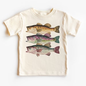 May include: A cream colored t-shirt with a graphic of three bass fish in different colors. The fish are arranged vertically, with the largest fish at the top and the smallest fish at the bottom. The fish are all facing to the right.