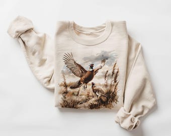 May include: A beige sweatshirt with a graphic print of two brown and white pheasants in a field of tall grass.