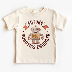 May include: Cream-colored t-shirt featuring a cartoon robot design. The robot is gray, orange, and yellow, with the words "FUTURE ROBOTICS ENGINEER" in a circular design around the robot. The shirt has short sleeves and a crew neck.