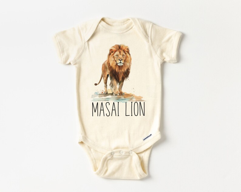 May include: A cream-colored baby onesie with a watercolor illustration of a lion standing in a puddle of water. The text "MASAI LION" is printed in black below the lion.