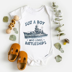 May include: White baby onesie with a blue and grey illustration of a battleship and the text "Just a boy who loves battleships".