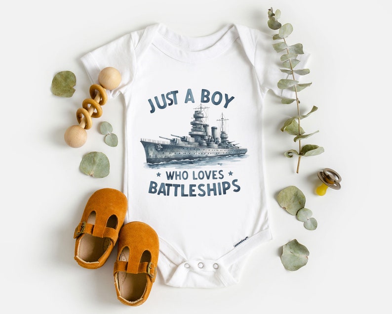 May include: White baby onesie with a blue and grey illustration of a battleship and the text "Just a boy who loves battleships".