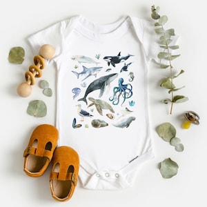 May include: White baby onesie with a colorful watercolor illustration of various sea creatures, including a whale, shark, octopus, sea turtle, and seahorse.