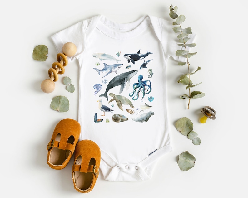 May include: White baby onesie with a colorful watercolor illustration of various sea creatures, including a whale, shark, octopus, sea turtle, and seahorse.