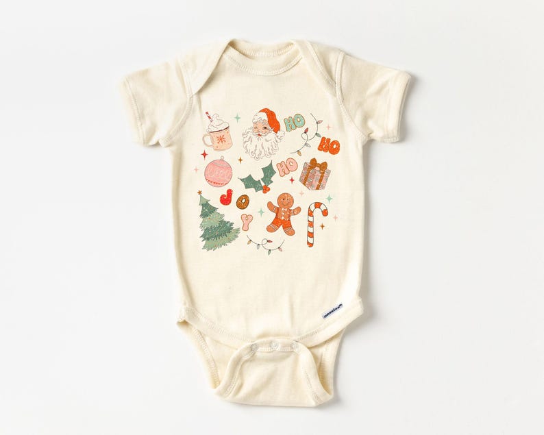Puede incluir: Body de beb&eacute; color crema con un dise&ntilde;o navide&ntilde;o festivo. El dise&ntilde;o incluye a Pap&aacute; Noel, un &aacute;rbol de Navidad, un hombre de jengibre, un bast&oacute;n de caramelo, adornos y la palabra "HO" en naranja. Tambi&eacute;n se muestra una taza de chocolate caliente y la palabra "JOY".