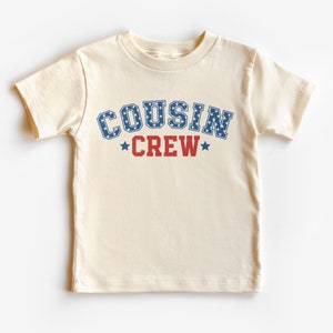 May include: A cream-colored t-shirt with a blue and red graphic that says "COUSIN CREW" with stars.
