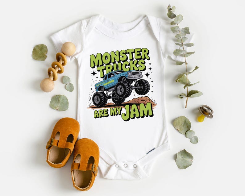 Puede incluir: Body de beb&eacute; blanco con un gr&aacute;fico de un cami&oacute;n monstruo azul y el texto "MONSTER TRUCKS ARE MY JAM" en verde y negro. La imagen incluye un par de zapatos de beb&eacute; naranjas y un juguete de madera.