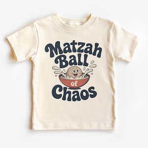 Peut inclure: T-shirt crème pour enfant avec l'inscription "Matzah Ball of Chaos" en bleu marine, avec une boulette de matzah de dessin animé dans un bol rouge. La boulette de matzah a un visage souriant et est entourée d'éclaboussures.