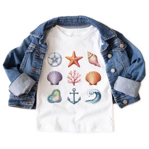 May include: White t-shirt featuring colorful illustrations of various sea creatures, including a starfish, seashells, and an anchor. The shirt is paired with a blue denim jacket, creating a casual and nautical theme. The design is suitable for children.