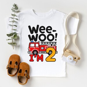 May include: White t-shirt with a red fire truck and the text "Wee-Woo! I'm 2" in black and yellow.