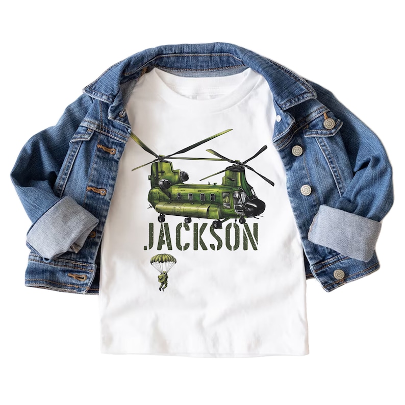 May include: White t-shirt with a green military helicopter and a parachuting figure. The text "JACKSON" is printed in a camouflage font below the helicopter.