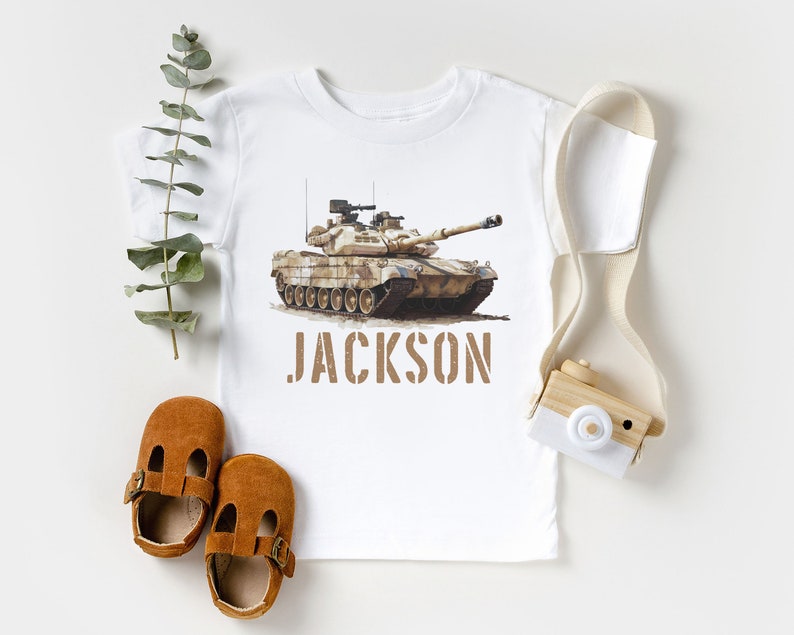May include: White t-shirt with a camouflage tank printed on the front. The tank is brown and green with a white background. The name "JACKSON" is printed below the tank in brown letters.