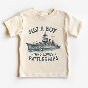 May include: A cream coloured t-shirt with a navy blue graphic of a battleship and the text "Just a boy who loves battleships".