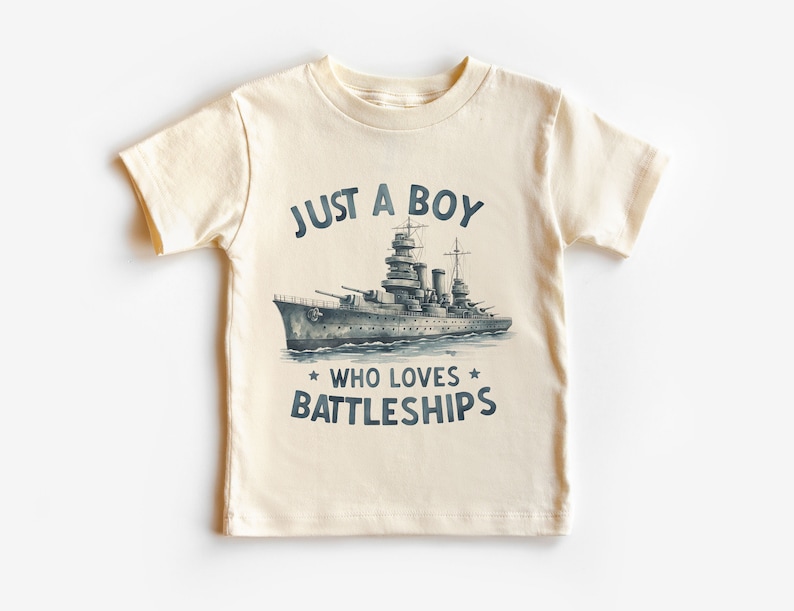 May include: A cream coloured t-shirt with a navy blue graphic of a battleship and the text "Just a boy who loves battleships".