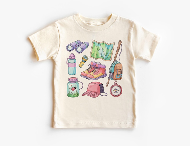 K&ouml;nnte beinhalten: Cremefarbenes T-Shirt mit einer farbenfrohen Illustration von Outdoor-Abenteuer-Ausr&uuml;stung. Das Design umfasst Fernglas, eine Karte, Wanderschuhe, einen Rucksack, einen Kompass, eine Wasserflasche, eine Taschenlampe, ein Glas mit einem Marienk&auml;fer und eine Baseballkappe.