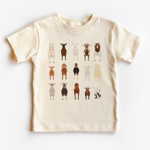 May include: A cream-colored t-shirt with a graphic of 15 goats in various poses and colors. The goats are all facing forward, with the exception of one goat that is upside down.