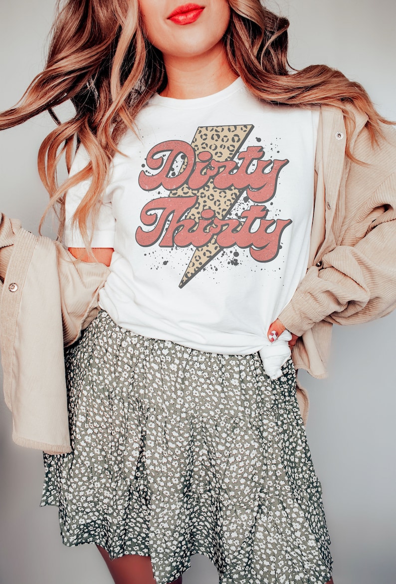 May include: White t-shirt with a red and yellow graphic that says "Dirty Thirty" with a leopard print lightning bolt.