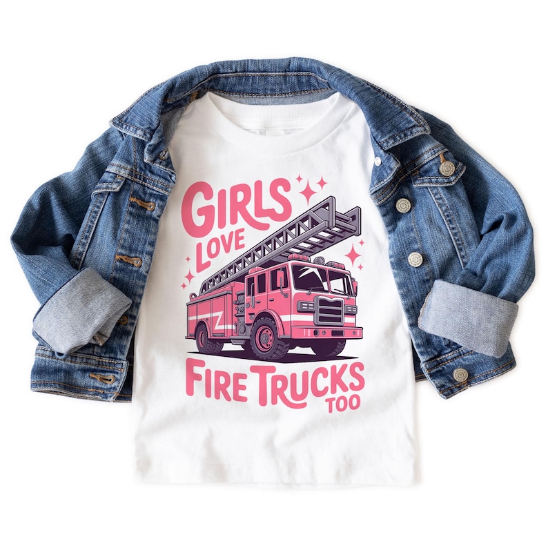 K&ouml;nnte beinhalten: Wei&szlig;es T-Shirt mit einem rosa Feuerwehrauto-Motiv und dem Text "GIRLS LOVE FIRE TRUCKS TOO". Eine blaue Jeansjacke liegt &uuml;ber dem T-Shirt.