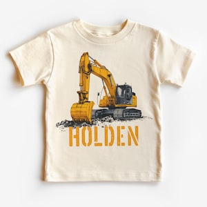Könnte beinhalten: Ein cremefarbenes T-Shirt mit einem gelben Bagger-Motiv und dem Namen "HOLDEN" in Orange.