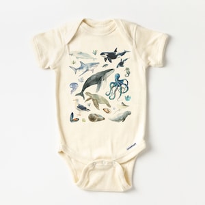 May include: A cream-colored baby onesie with a watercolor print of various sea creatures, including a whale, shark, octopus, sea turtle, and seagull.