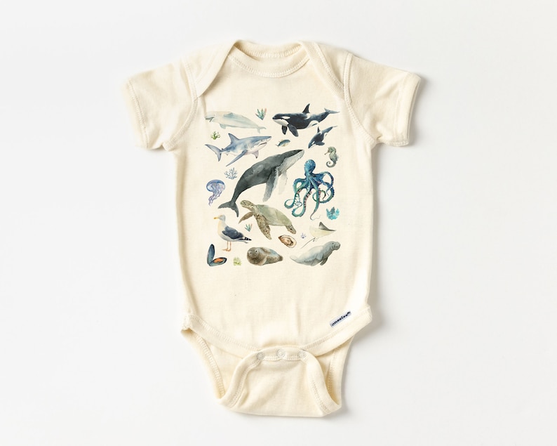 May include: A cream-colored baby onesie with a watercolor print of various sea creatures, including a whale, shark, octopus, sea turtle, and seagull.