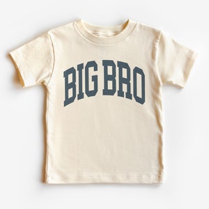 May include: A cream colored short-sleeved t-shirt with the text "BIG BRO" in a navy blue arch.