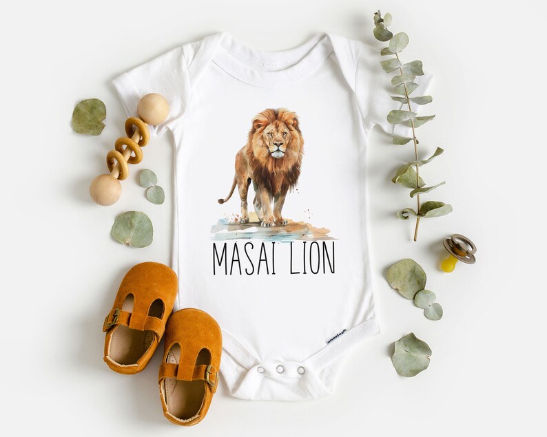 May include: White baby onesie with a watercolor illustration of a lion with the text "MASAI LION" printed below.