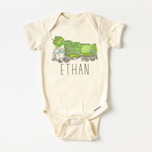 May include: A cream-colored baby onesie with a green and white garbage truck illustration and the name "ETHAN" printed in black.