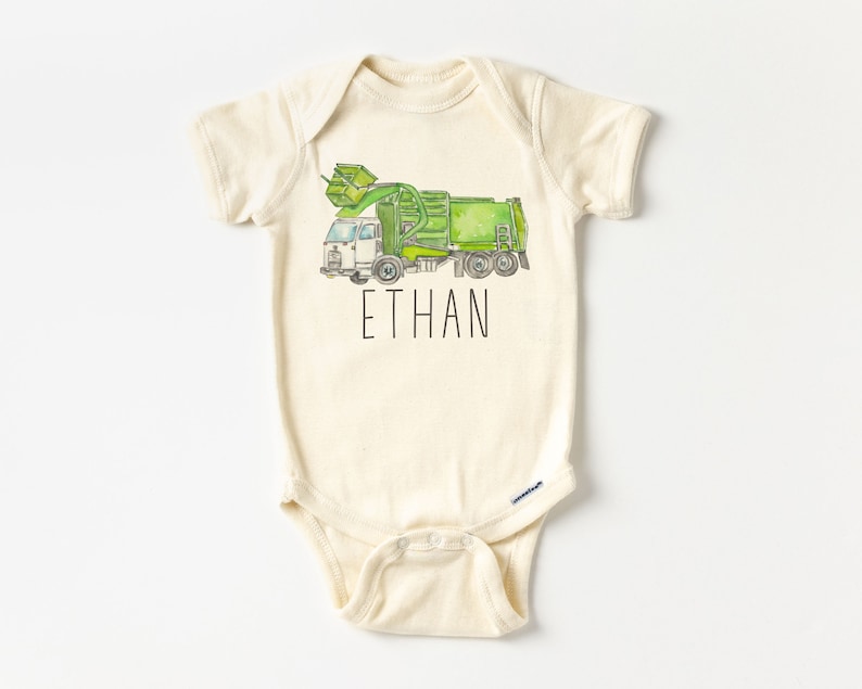 May include: A cream-colored baby onesie with a green and white garbage truck illustration and the name "ETHAN" printed in black.