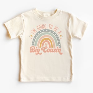 以下が含まれることがあります： 虹のデザインと「I'm going to be a Big Cousin」というテキストが書かれた白いTシャツです。