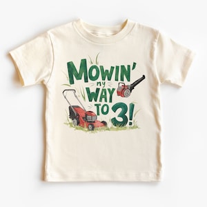 May include: A white t-shirt with a green and red graphic of a lawnmower and leaf blower. The text on the shirt reads "Mowin' my way to 3!"