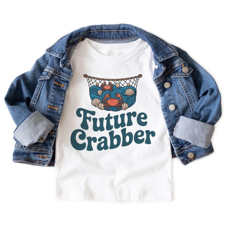 May include: White t-shirt with a blue denim jacket. The t-shirt features a graphic of crabs, seashells, and waves inside a net, with the text "Future Crabber" in teal.