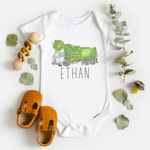May include: White baby onesie with a green and white garbage truck illustration and the name "ETHAN" printed below.