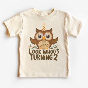 Op de afbeelding: Een beige T-shirt met korte mouwen met een bruine uil die een feestmuts draagt en de tekst "Look Whoo's Turning 2".