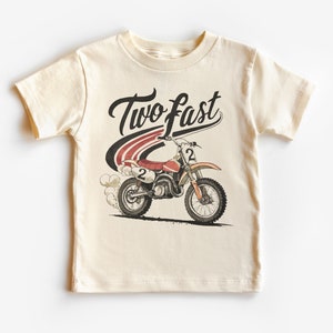 May include: A cream colored t-shirt with a vintage style graphic of a dirt bike with the text "Two Fast" above it.