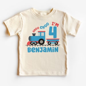 May include: A cream-coloured t-shirt with a blue train design and the text "choo choo I'm 4" in red and blue. The name "Benjamin" is printed in blue below the train. The shirt is for a child's fourth birthday.